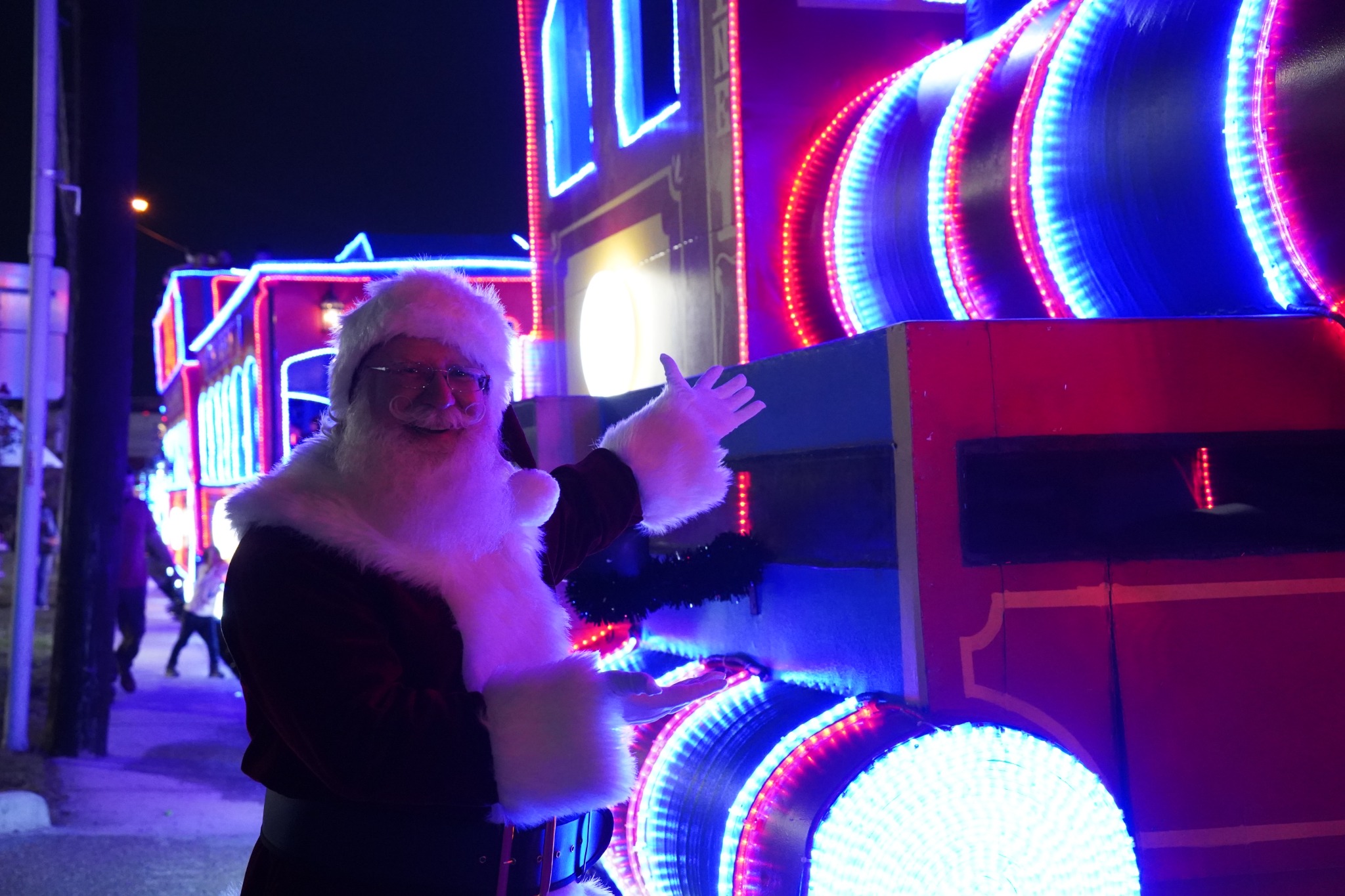 Santa Jangle beside a bright Christmas train display